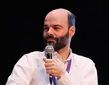 Un homme chauve et barbu tient un micro.