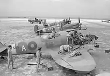 Des militaires en train d'entretenir des avions, sur une piste rudimentaire.