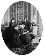 Photographie de trois femmes et d'un homme vêtus de noir et se recueillant devant la statue du buste d'un homme.