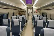 Photo couleur montrant un intérieur de train de couleur crème, sol, parois et plafond et sièges individuels bleu à têtière blanche.