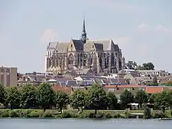 Basilique vue depuis le parc d'Isle avec, au premier plan, la Somme bordée d'arbres et, au loin, des maisons de briques rouges.