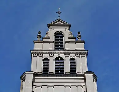 Parties supérieures de la tour avec une croix surmontée d'un coq dorée et, un peu plus bas, deux têtes sculptées de saint Quentin avec les clous sur chaque épaule.
