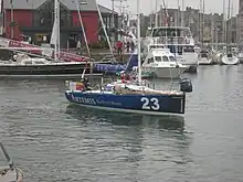 Voilier bleu s'éloignant du quai au moteur.