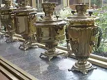 Une rangée de samovars cuivrés devant une fenêtre.