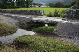 Vue d’un pont rustique formé d’une grande lauze sur un ruisseau.