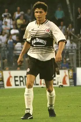 Photographie d'un joueur de football vu de face, marchant, avec un maillot blanc rayé de noir.