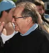 Photographie d’un homme avec des lunettes souriant en train d’échanger avec un individu qu’on ne voit pas.