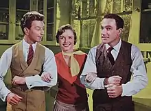 Sur un fond de cuisine filtré en jaune, les trois acteurs principaux du film. À gauche, Cosmo regarde Don. Kathy, qui prend le bras de ses deux compagnons, sourit à la caméra, comme Don sur la droite.