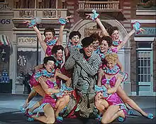 Gene Kelly souriant, entouré de femmes habillées de roses et enthousiastes.