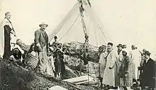Carte postale ancienne représentant un groupe de personnes autour d'une installation destinée à faire sortir un sarcophage en forme de femme d'un puits funéraire.