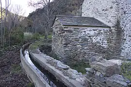 Petit canal en eau. Sur sa droite, bâtiment en pierre surmonté d'un toit de lauzes.