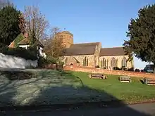 Photo d'un bâtiment allongé flanqué d'une tour carrée crénelée à moitié masquée par un arbre. Au premier plan, un petit carré d'herbe avec quelques bancs