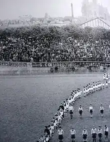 Défilé d'athlètes devant une tribune pleine de spectateurs.