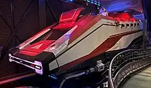 Personnes attendant devant un écran et un vaisseau spatial blanc et orange.