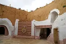 Photo d'une maison taillée dans la roche avec des soubassements blancs.