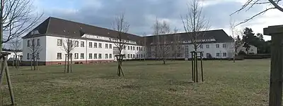 Photographie en couleur d'un bâtiment de deux étages à deux ailes perpendiculaires, entouré d'une pelouse rase.
