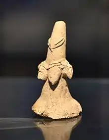Figurine en terre cuite qui représente une femme. La forme générale est triangulaire et les yeux sont en amande.