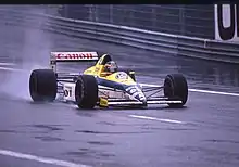 Photo d'une monoplace jaune, blanche et bleue sur une piste détrempée.