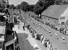 Photographie en noir et blanc montrant le passage d'une course cycliste dans un village néerlandais.