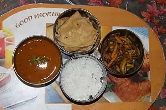 Un tiffin ouvert : quatre mets du repas gujaratis  : (dans le sens des aiguilles d'une montre à partir de la gauche) daal (soupe de lentilles), rotli (pain plat), shaak (légumes cuits), bhat (riz)