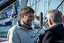 Portrait, de trois-quarts. Il converse avec un homme vu de dos.