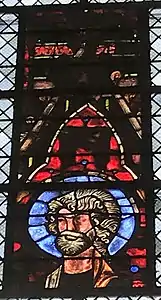 Vitrail avec des teintes dominantes rouges et bleues représentant, en sa partie inférieure, un homme barbu pourvu d'une auréole.