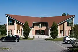 Vue d'un bâtiment moderne en brique, toiture à facettes de part et d'autre du porche d'entrée.