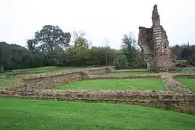 Photographie en couleurs de murs ruinés sur une esplanade engazonnée.