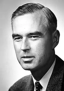 Photo en noir et blanc. Torse d'un homme au cheveux noir portant un complet.