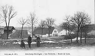 Photo noir et blanc de d'un bâtiment possédants une importante toiture à coté d'ancienne fermes en contrebas d'une route.