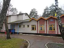 Photographie en couleurs. Bâtiments partiellement colorés. Présence de végétation aux abords. Temps humide, ciel couvert.