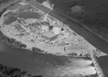 Photo aérienne en noir et blanc, les deux bâtiments cylindriques des réacteurs sont au centre de la photo.