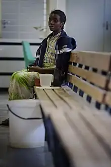 Photo d'une femme assise au bout d'un banc en bois qui attend, l'air résigné.