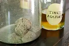 Deux récipients en verre contenant, au premier plan, des morceaux de résine avec déchets végétaux, et au second plan, une teinture de couleur jaune orangé.