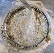 Gros plan sur un récipient en métal rempli d'une substance épaisse de couleur beige mélangée par une lame en métal.