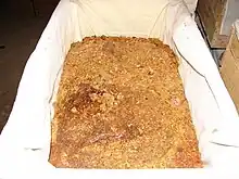 Plan rapproché d'une caisse en bois garnie de tissu blanc et remplie de résine en morceaux de tailles variées de couleur jaune clair à brun foncé.