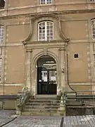 Un escalier de six marches conduit à une porte dont l'encadrement est orné par deux colonnes surmontée d'un fronton.