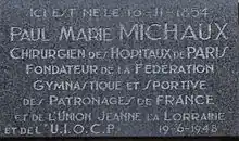 Photo de la plaque commémorative apposée sur la maison natale de Paul Michaux avec, pour inscription : « Ici est né le 16-11-1854 Paul Marie Michaux, Chirurgien des Hôpitaux de Paris Fondateur de la Fédération Gymnastique et Sportive des Patronages de France et de l’Union Jeanne la Lorraine et de l’U.I.O.C.P 19-6-1948 ».